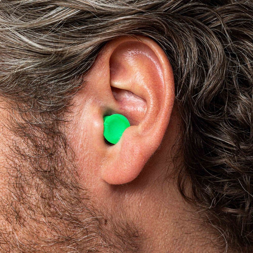 Un bouchon d'oreille dans une oreille. Le bouchon vert est visible. L'oreille est en gros plan.
