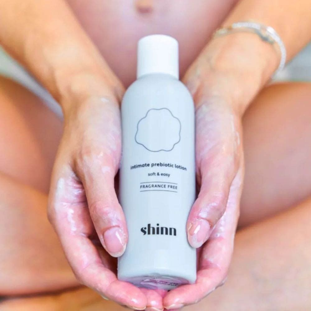 Personne tenant une bouteille. Blanc, logo rose. Texte : "intimate prebiotic lotion".