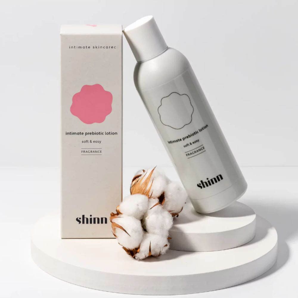 Fles en verpakking. Wit, roze logo. Katoen ernaast. Tekst: "intimate prebiotic lotion". 