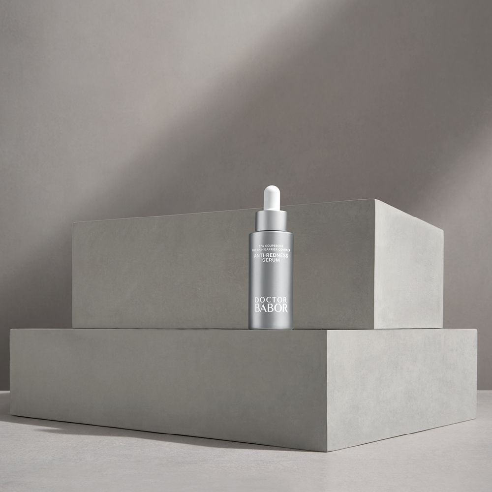 Un flacon argenté sur des blocs gris. Inscription: Anti-Redness Serum, Doctor BABOR.