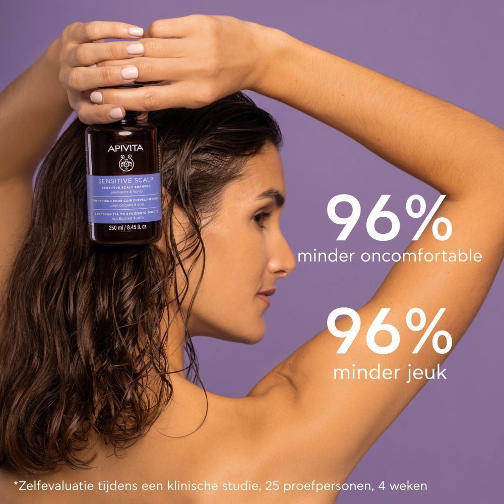 Vrouw houdt shampoo fles vast. Tekst: Apivita Sensitive Scalp Shampoo. 96% minder oncomfortabel.