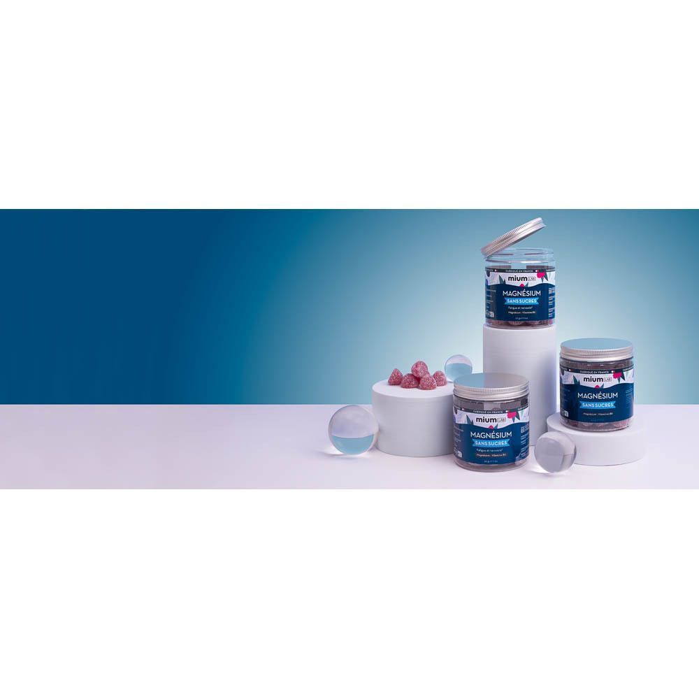 Drie potten MiumLab Magnesium op sokkels. Open deksels. Blauwe etiketten met witte tekst. Achtergrond: blauw en wit.