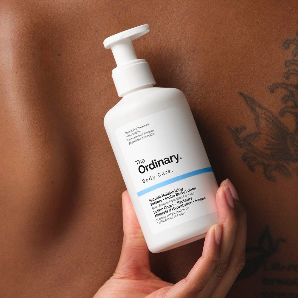 Flacon blanc avec pompe. Inscription : The Ordinary, Body Care, Natural Moisturizing Factors + Inulin Body Lotion. Tenue à la main.