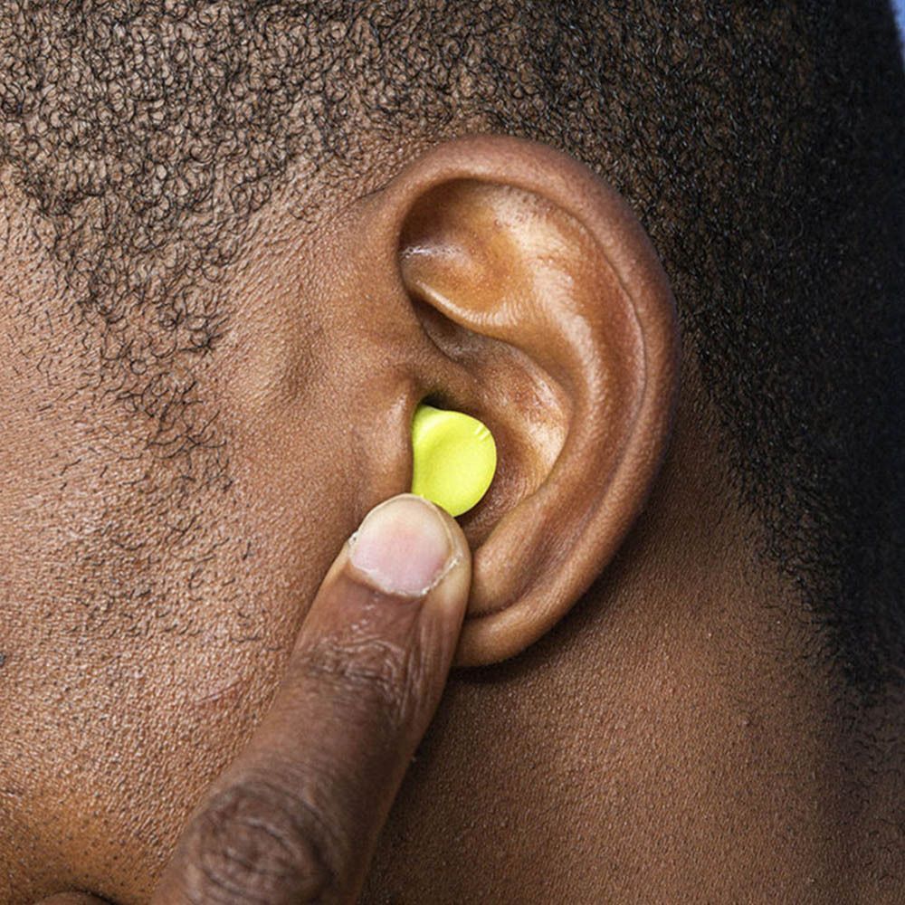 Personne avec un bouchon d'oreille jaune dans l'oreille. Le doigt touche le bouchon d'oreille. Couleur de peau.