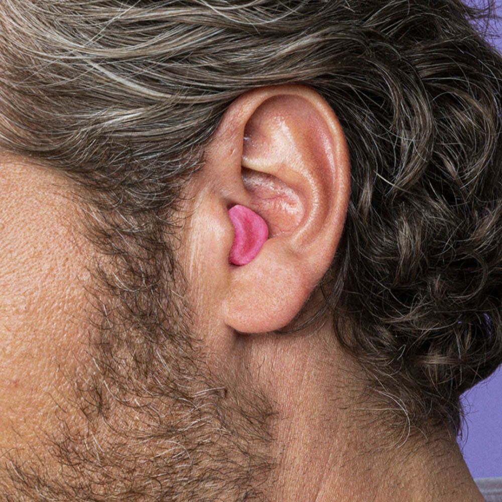 Oreille d'un homme avec un bouchon d'oreille rose. Le bouchon est placé dans l'oreille.