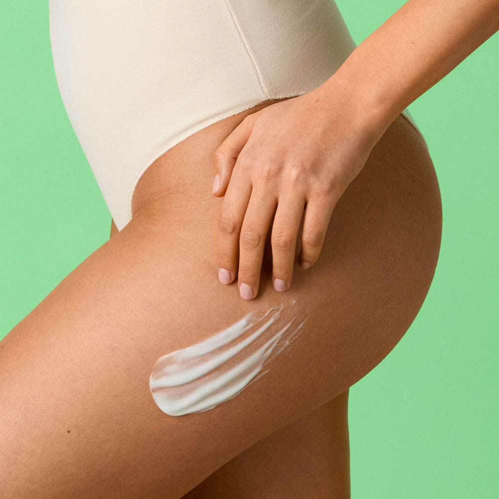 Persoon in witte badpak. Crème wordt aangebracht op de dij. Achtergrond: groen.
