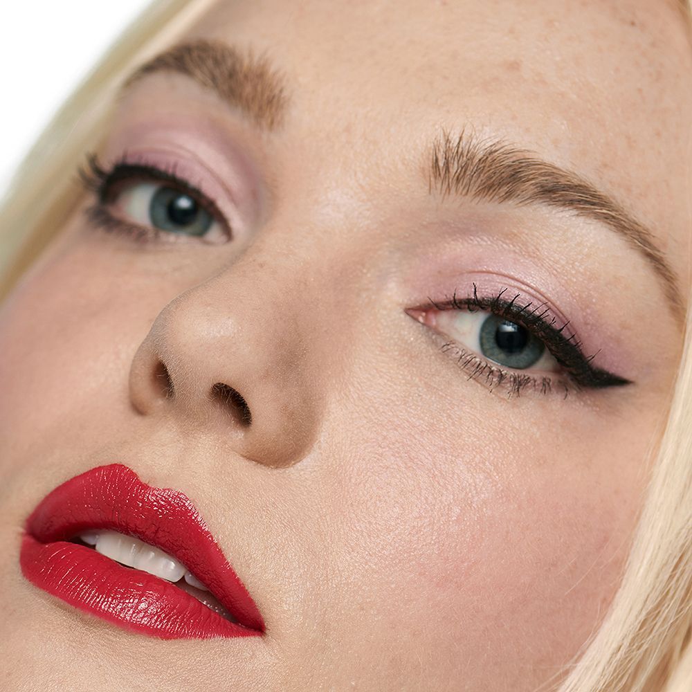 Portret van een vrouw met make-up, rode lippen, die Clinique Quickliner for Brows gebruikt.