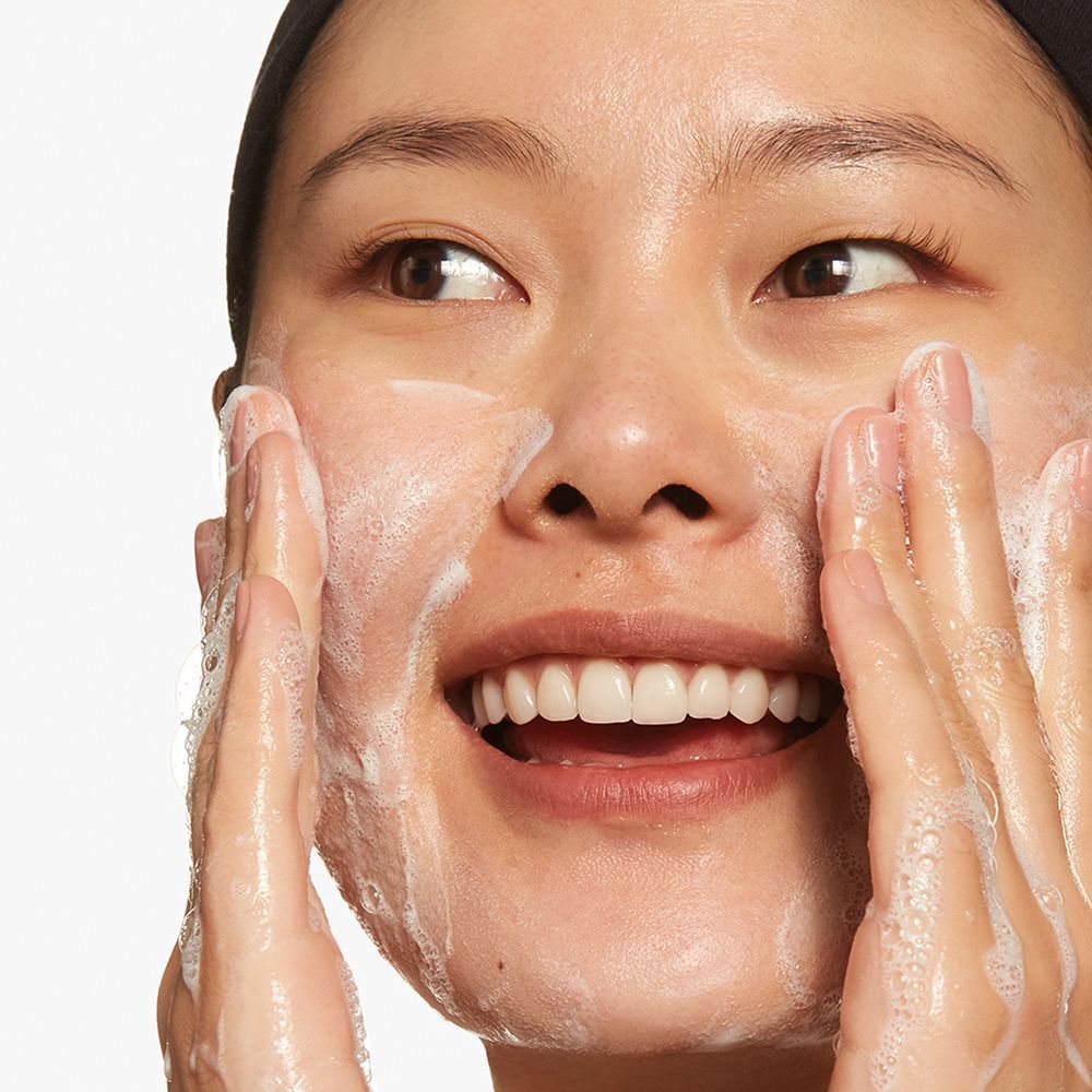 Une femme applique du gel nettoyant moussant sur son visage.