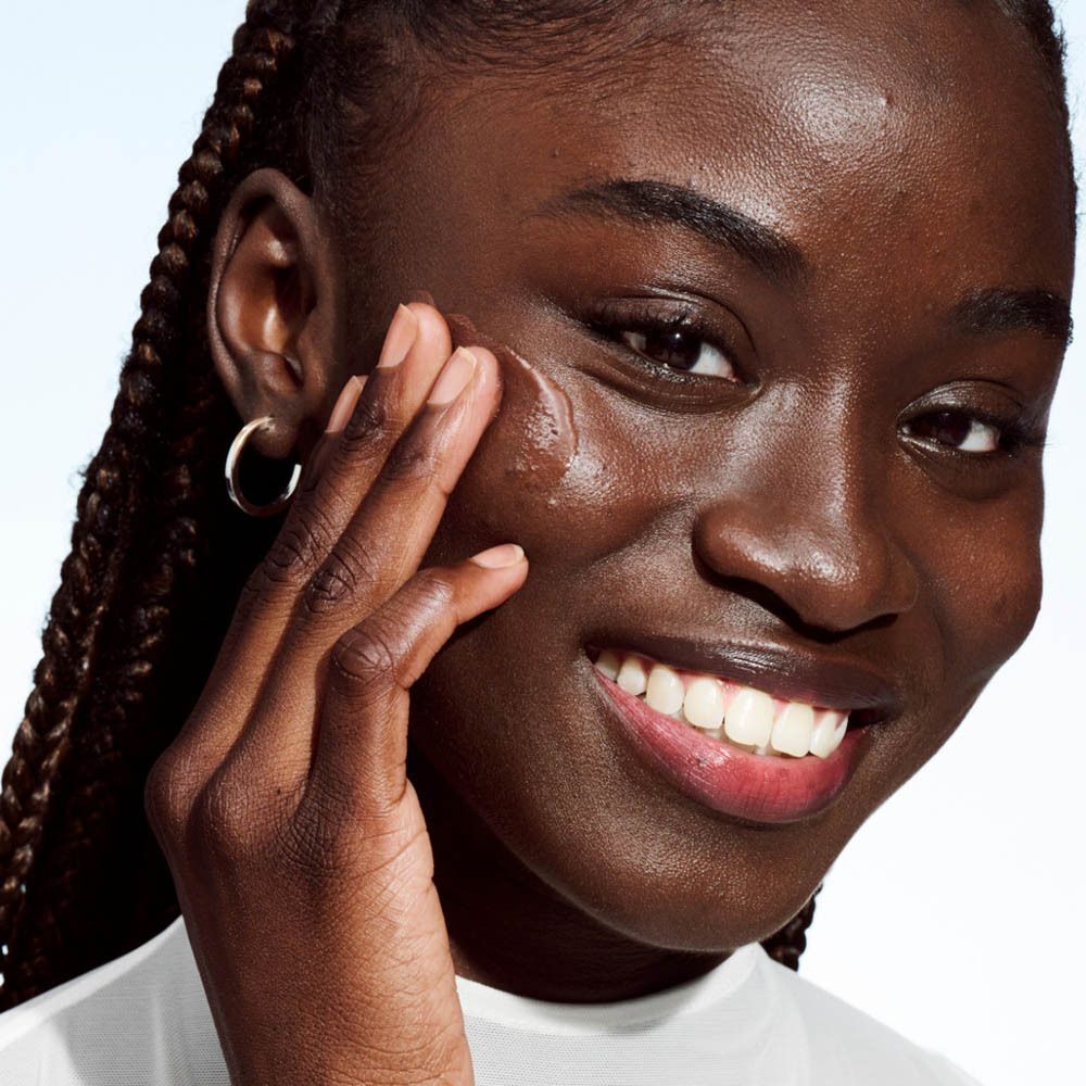 Close-up van een vrouw die Clinique Even Better Clinical™ Vitamin Makeup SPF 50 op haar gezicht aanbrengt. Beige make-up.