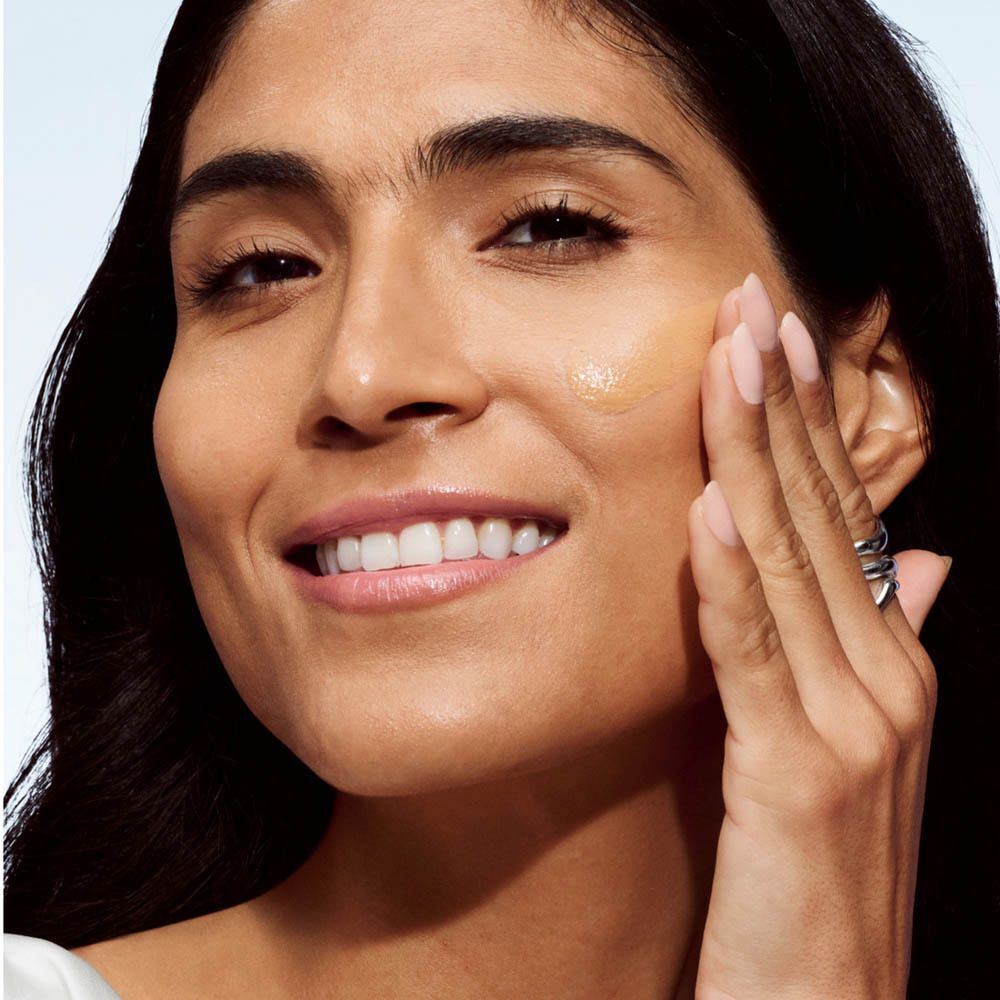 Femme appliquant Clinique Even Better Clinical Vitamin Makeup SPF 50. Peau moyenne, produit appliqué sur la joue.