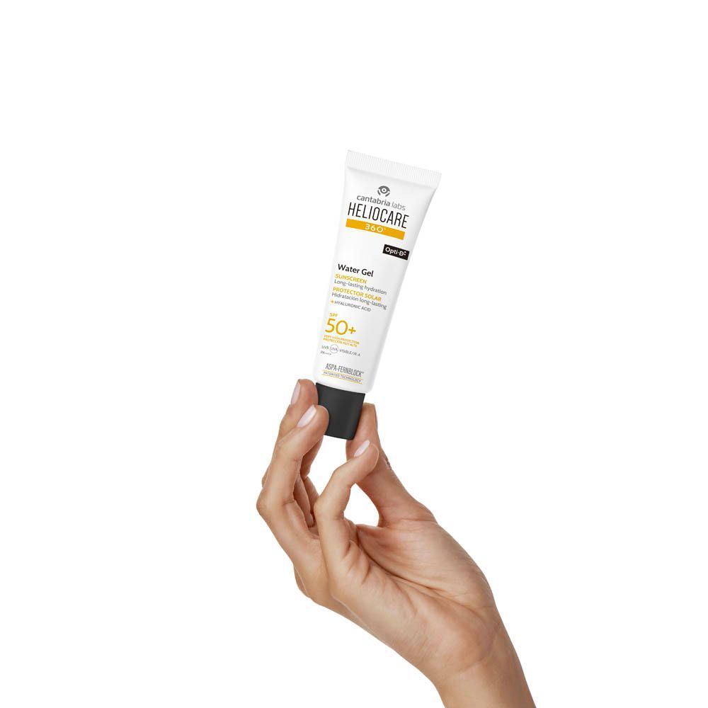Hand houdt tube Heliocare 360° Water Gel SPF50+. Witte tube met zwarte dop. Tekst: Heliocare 360°, Water Gel, SPF50+.