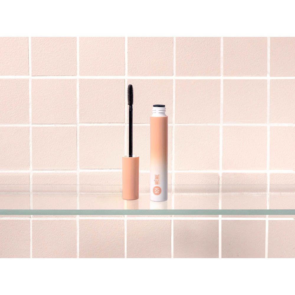 Mascaratube en borstel op glazen plank. Roze tegels op de achtergrond.