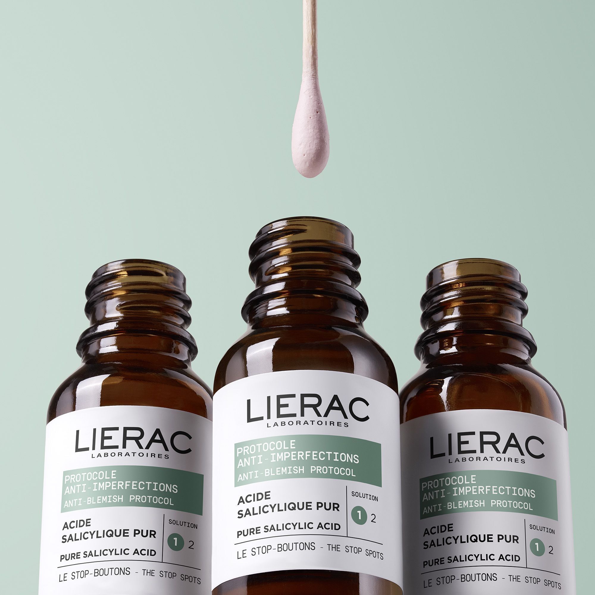 Trois flacons bruns avec bouchon noir. Coton-tige avec produit. Marque : Lierac.