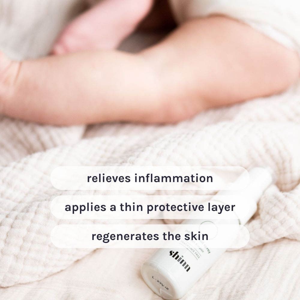 Witte intieme olie spray naast babyvoetjes op witte stof. Tekst: verlicht ontstekingen, beschermt, regenereert de huid.
