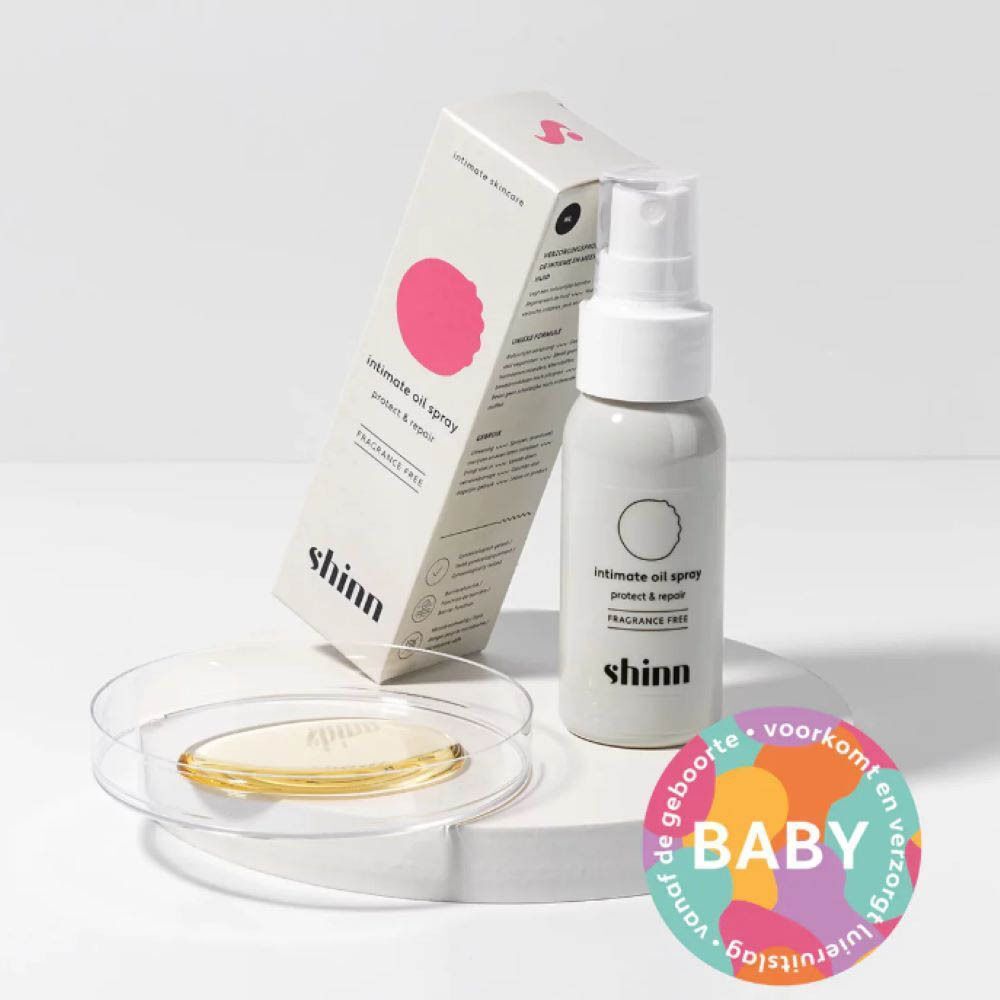 Witte intieme olie spray en verpakking. Product op glazen plaat met gele vloeistof. Baby label.