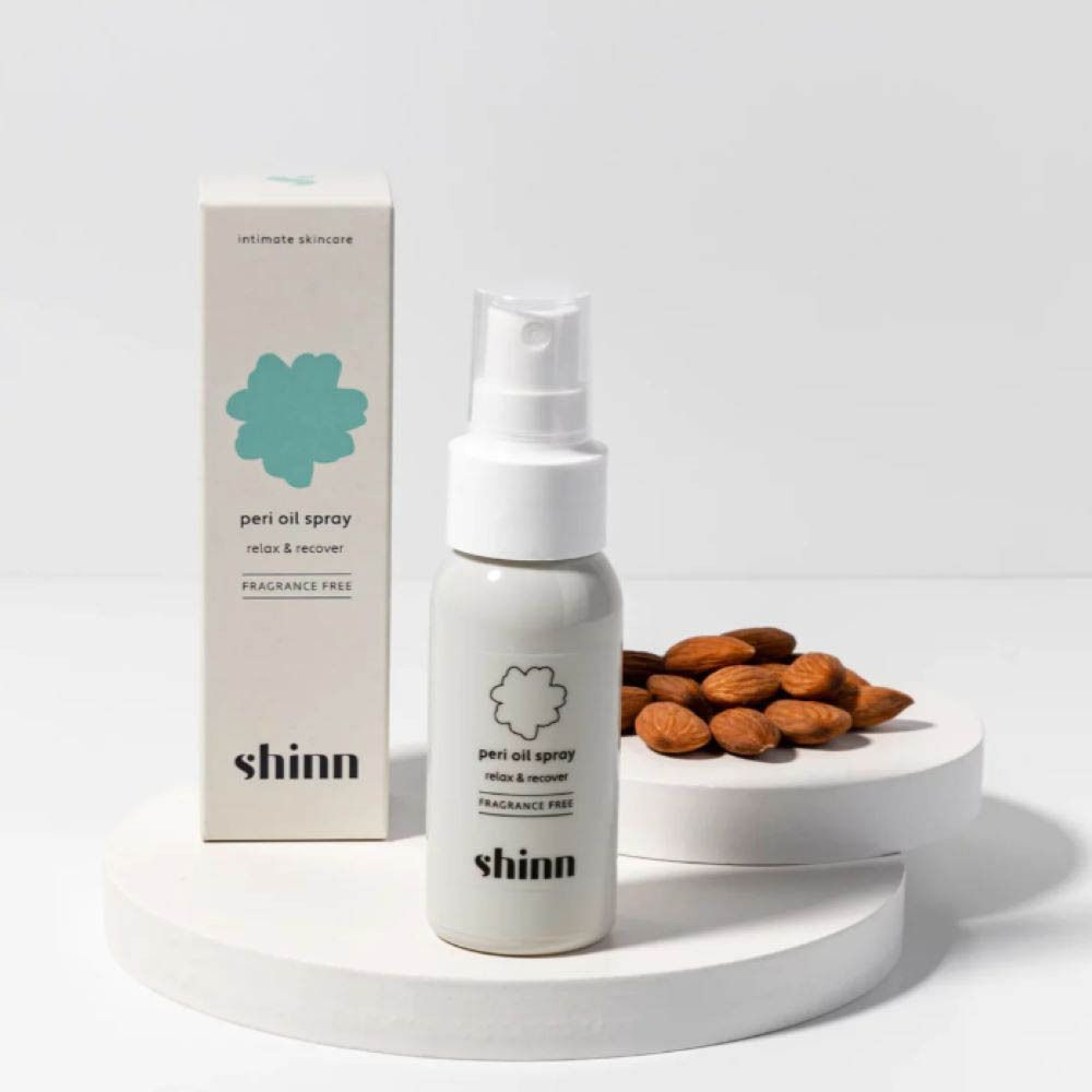 Flacon pulvérisateur blanc et boîte. Texte : Shinn, Peri Oil Spray, relax & recover, sans parfum. Amandes sur un piédestal.