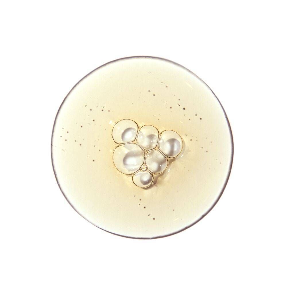 Druppels van de oplossing met kleine belletjes en glinsterende deeltjes op een rond oppervlak.