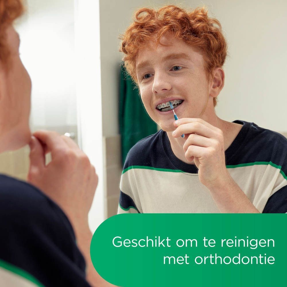 Jongeman poetst tanden met een blauwe GUM® TRAV-LER® rager voor een spiegel. Met beugel.