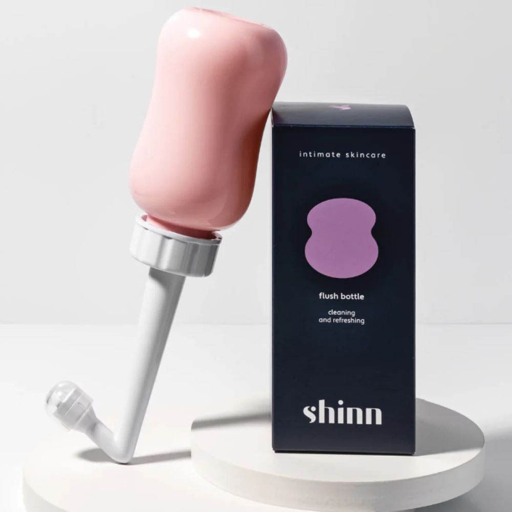 Flacon rose avec embout et emballage noir. Emballage avec symbole violet et texte: Soin intime de la peau, flacon de rinçage.