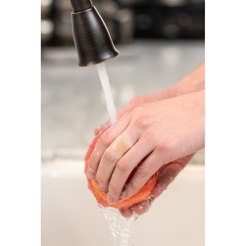 Een persoon wast een appel onder stromend water, met een pleister op de vinger.