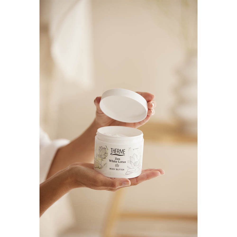 Handen houden een open witte pot Therme Zen White Lotus Body Butter vast. Deksel ernaast.