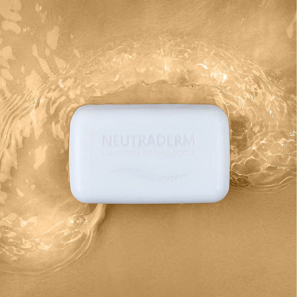 Neutraderm Dermo-Protecteur Savon Doux Surgras zeep, wit, rechthoekig, op gouden achtergrond met water.