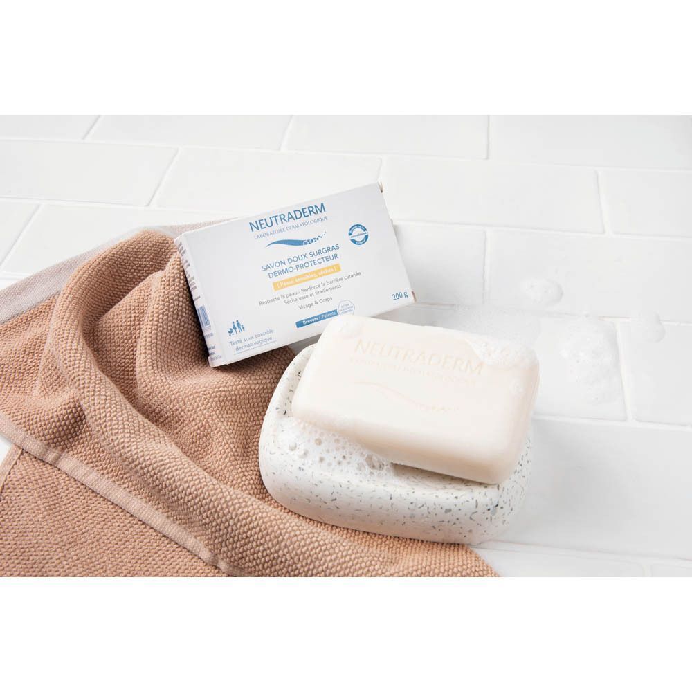 Savon et emballage Neutraderm Dermo-Protecteur Savon Doux Surgras sur une serviette et porte-savon. Fond carrelé.