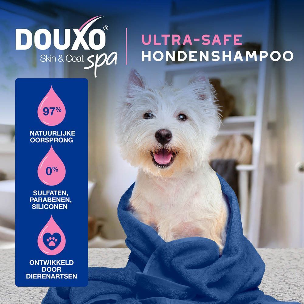 Een witte hond in een blauwe handdoek. Tekst: Ultra-veilige hondenshampoo. 97% natuurlijke oorsprong.