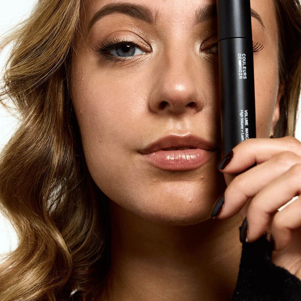 Vrouw houdt mascaratube voor haar gezicht. Productnaam zichtbaar.