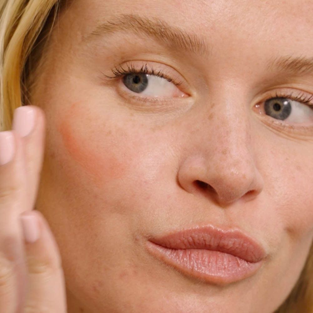 Femme avec produit rose sur la joue. Elle touche sa joue.