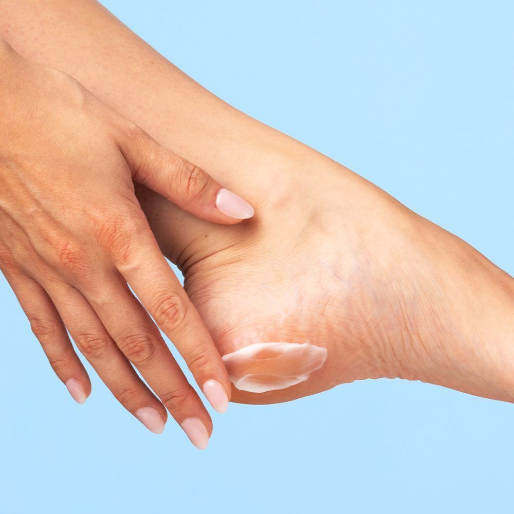 Close-up van een hand die crème op een hiel aanbrengt. Crème zichtbaar op de huid. Blauwe achtergrond.