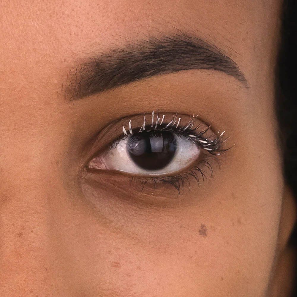 Gros plan sur un œil avec une base de mascara blanche sur les cils.