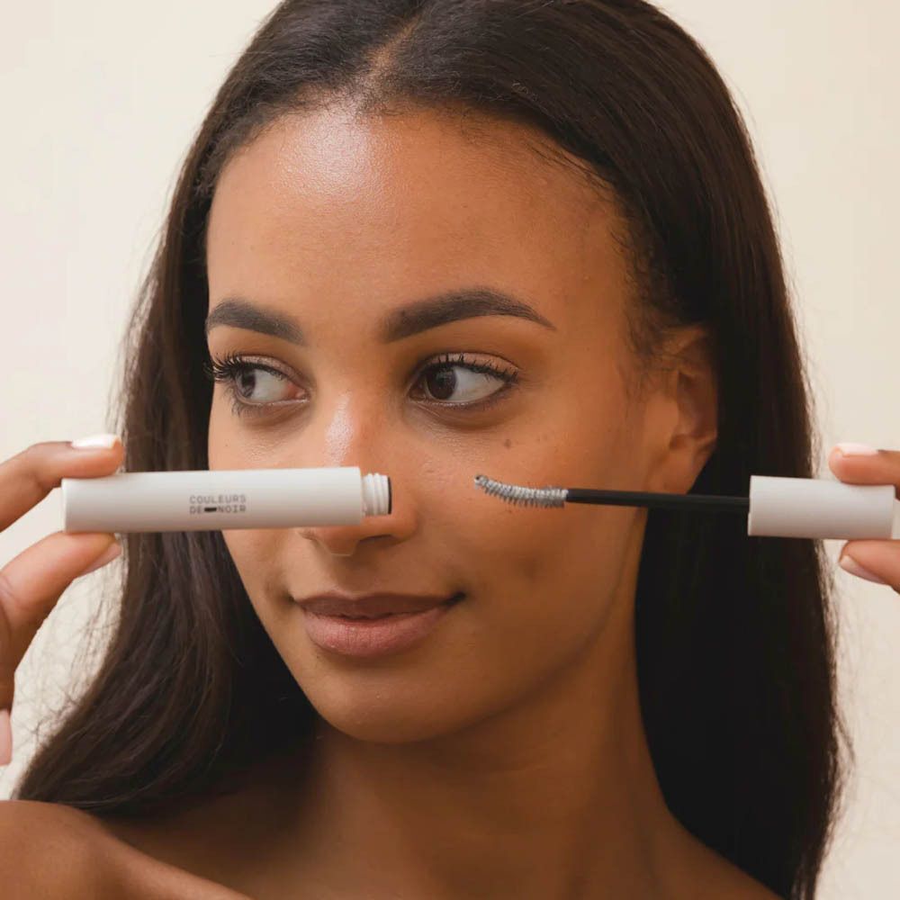 Personne tenant un tube de mascara et la brosse. Le capuchon est retiré.