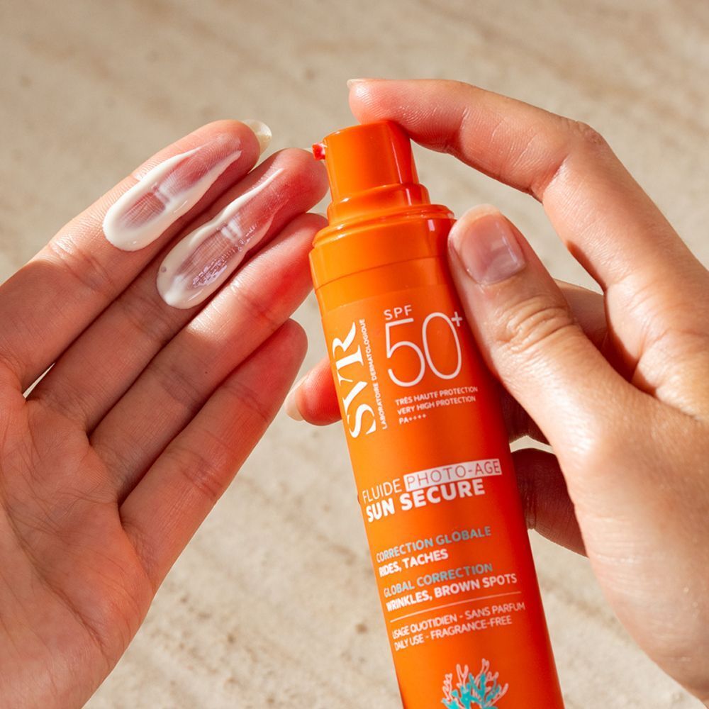 Mains tenant un flacon orange de SVR Sun Secure Fluide Photo-Age SPF50+. De la crème est présente sur la paume.