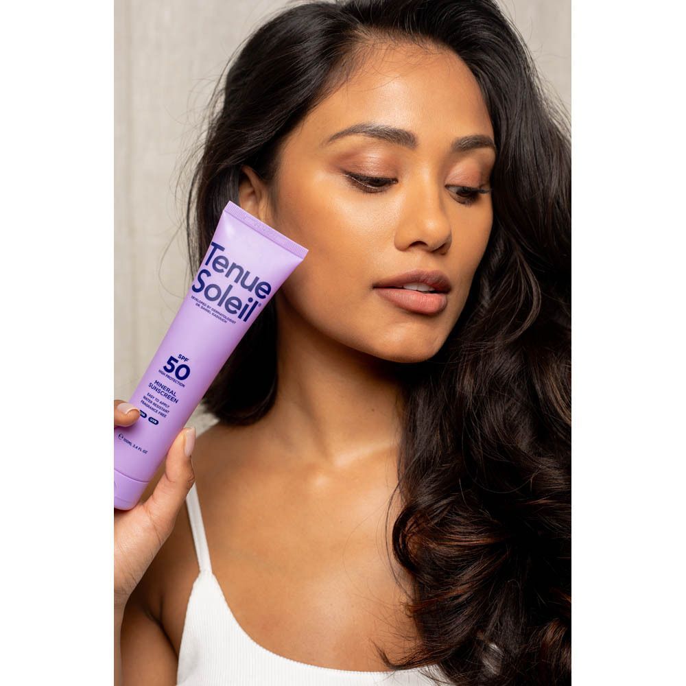 Femme tenant un tube de crème solaire violet. Inscription : Tenue Soleil, SPF 50. Femme regarde.