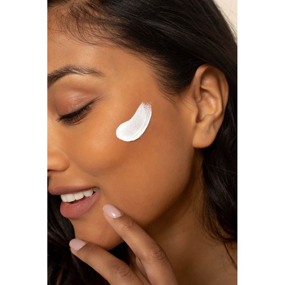 Gros plan d'une femme appliquant de la crème solaire sur son visage. Crème visible.