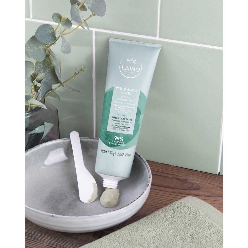 Een tube Laino Pâte Argile Verte, naast een kom en een spatel. Product geplaatst op een groene tegel.