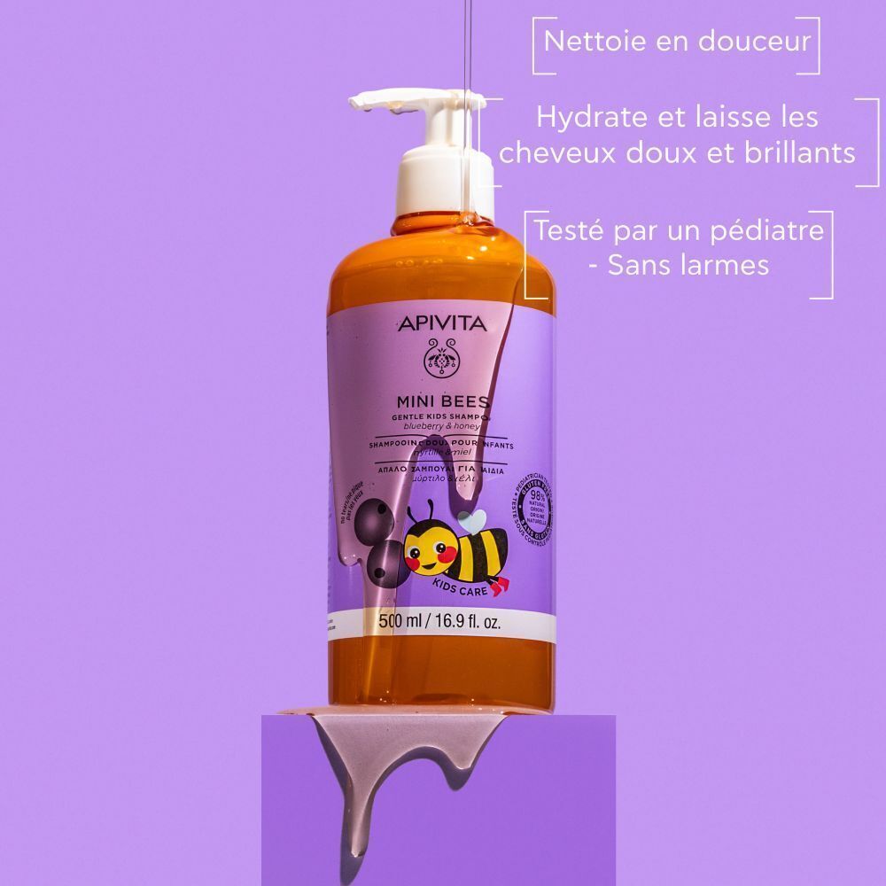 Flacon de shampooing Apivita Mini Bees. Étiquette violette, nom du produit, illustration d'abeille. Flacon sur socle.
