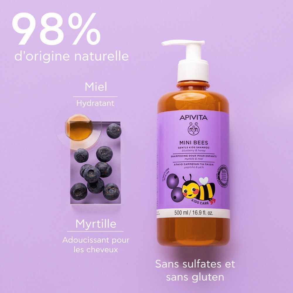 Flacon de shampooing Apivita Mini Bees à côté de myrtilles et miel. Étiquette violette, nom du produit, abeille.