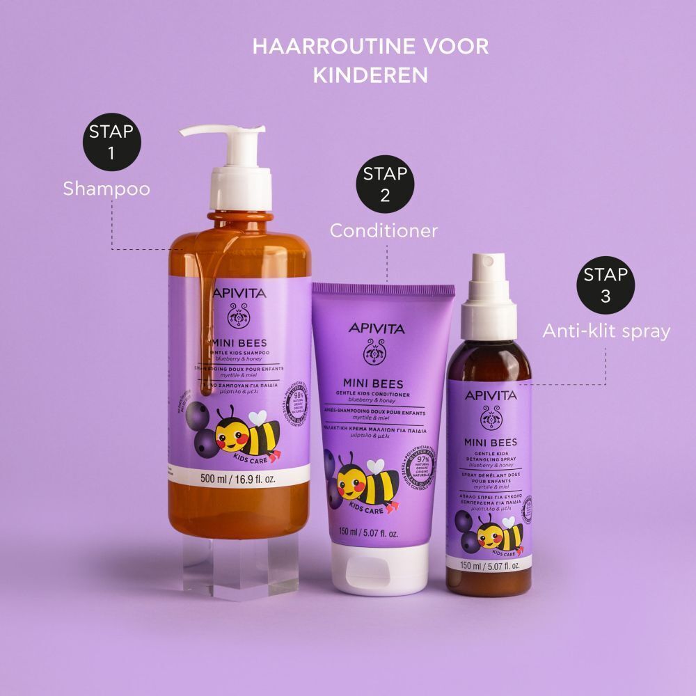 Hand houdt Apivita Mini Bees shampoo fles vast. Paars etiket, productnaam, bij. Bosbessen op de achtergrond.