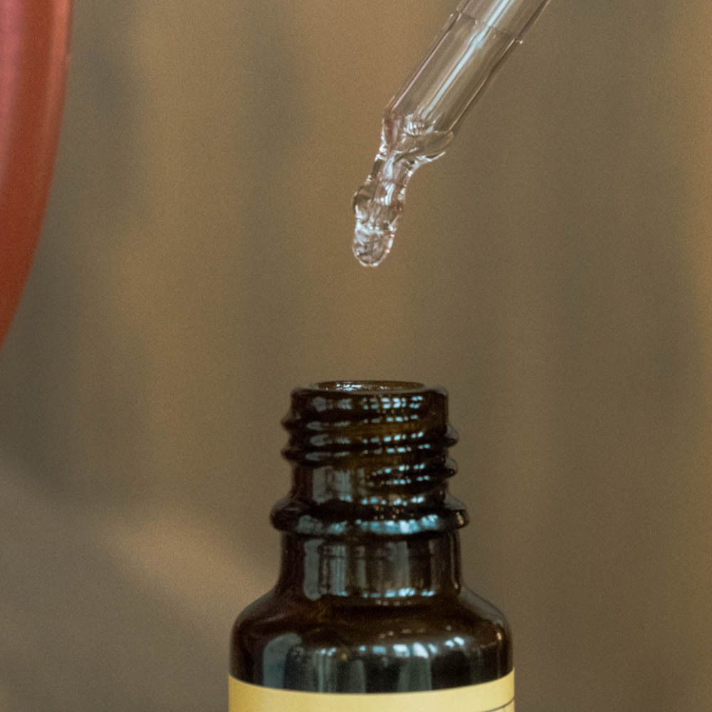 Close-up van een pipet die druppelt boven een fles Guud vitamine D. Bruine glazen fles.
