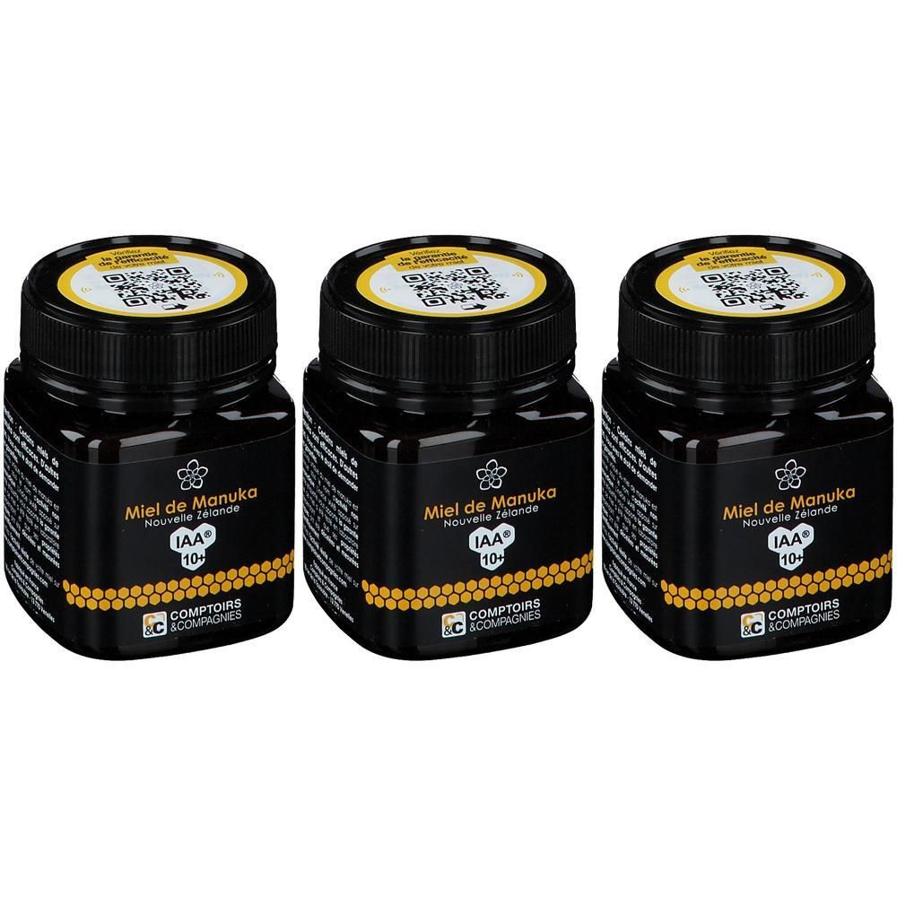 Trois pots de miel de Manuka IAA 10+. Pots noirs, couvercles noirs et étiquettes jaunes. Logo et code QR visibles.