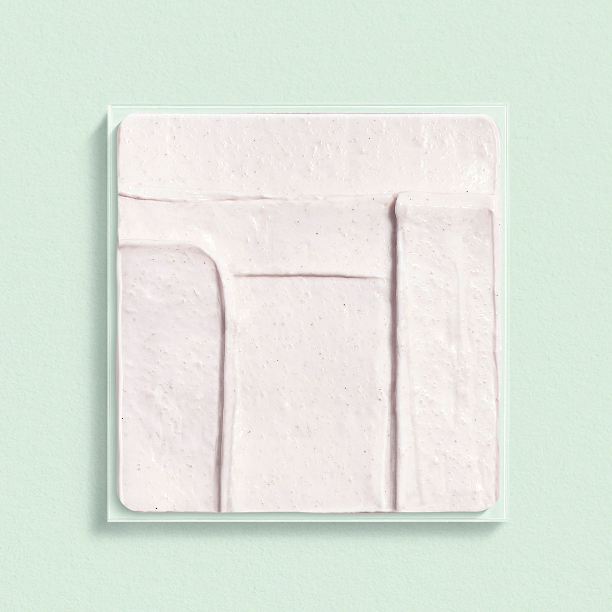 Échantillon carré de crème rose sur une surface verte.