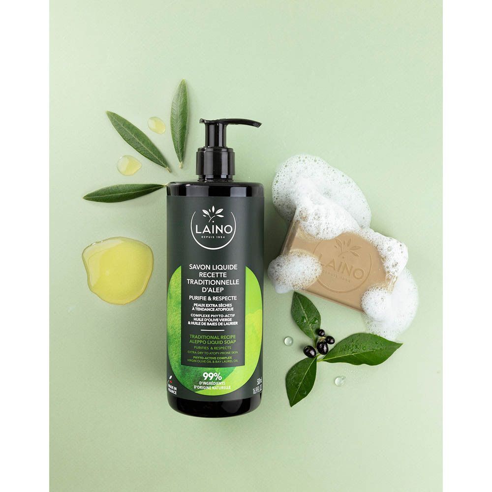 Flacon vert foncé avec pompe noire, entouré de feuilles et mousse de savon. Petit morceau de savon.
