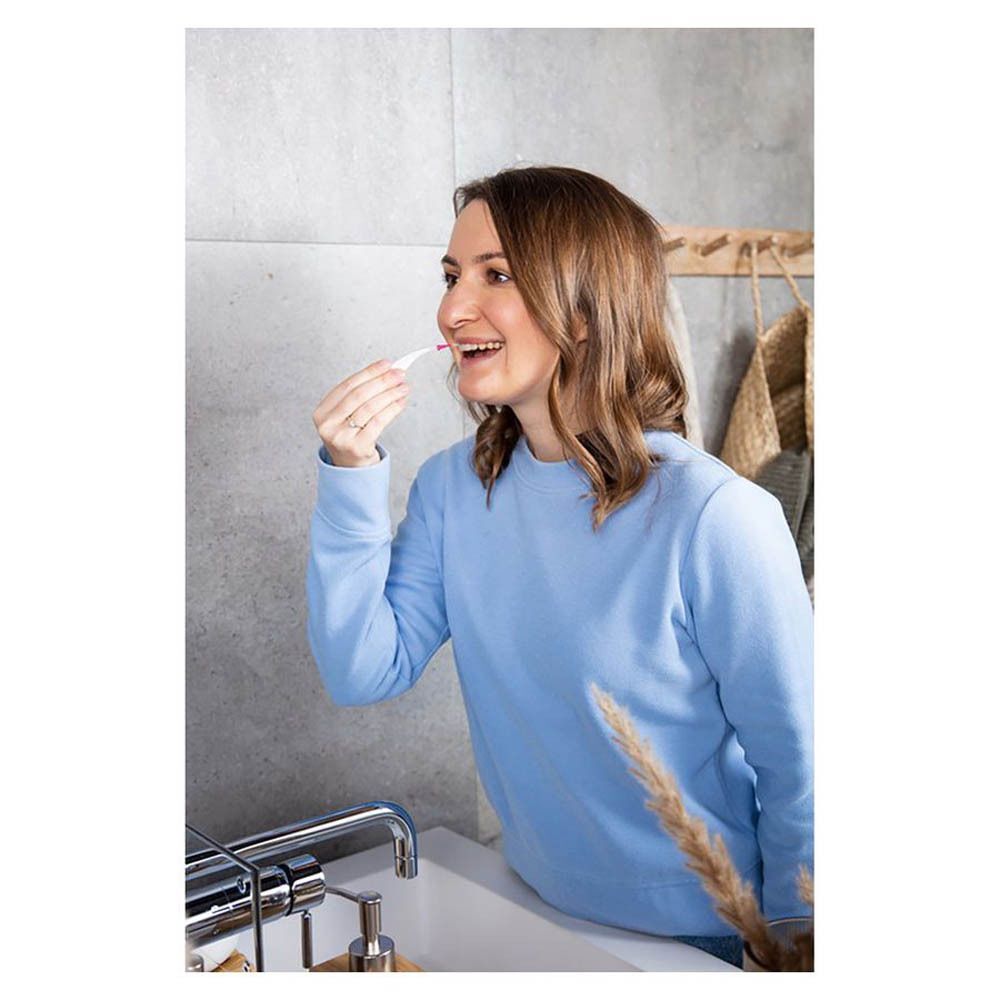 Femme dans une salle de bain utilisant une brossette interdentaire rose. Elle se tient devant un lavabo.