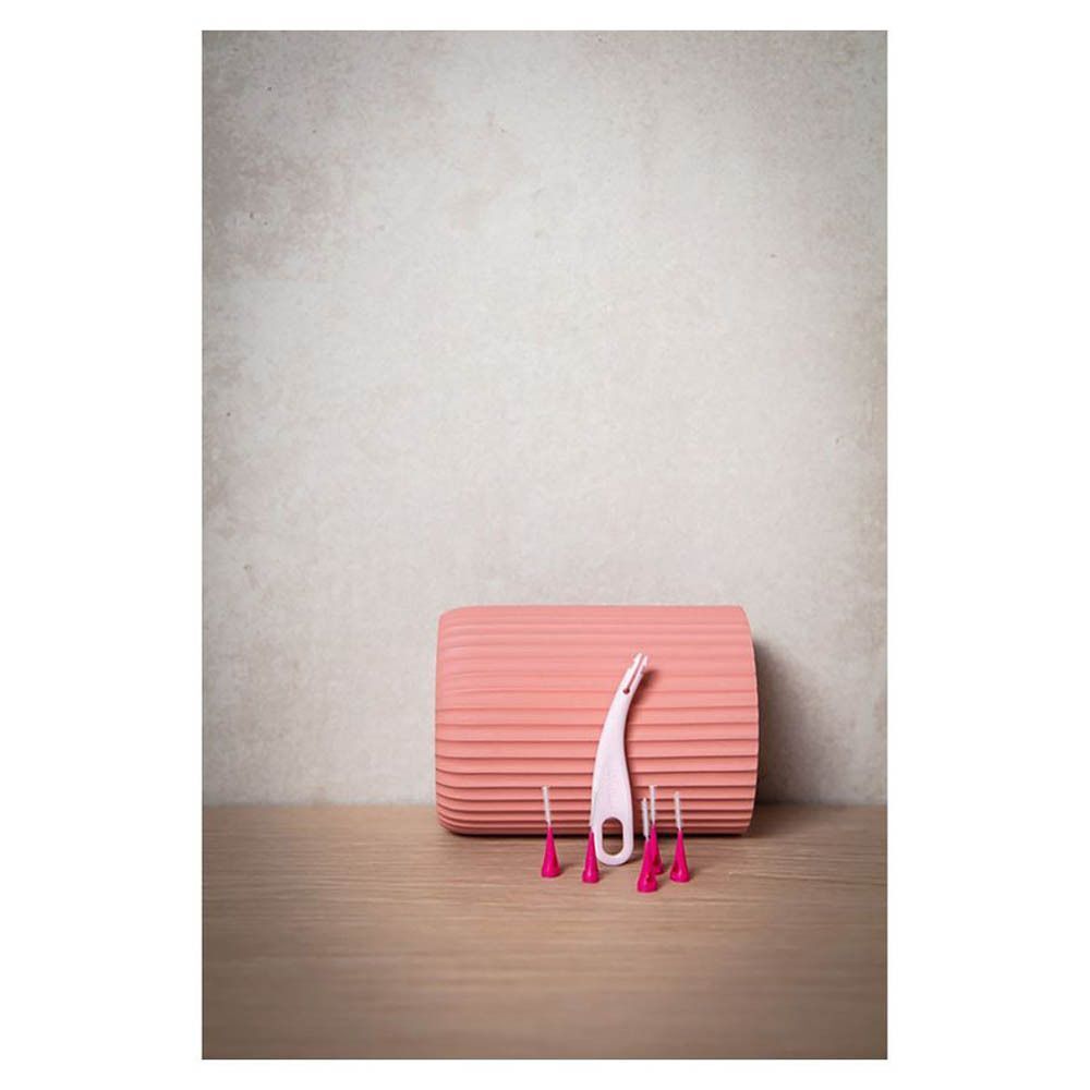 Brossette interdentaire rose et recharges posées sur une table, à côté d'un récipient cannelé.