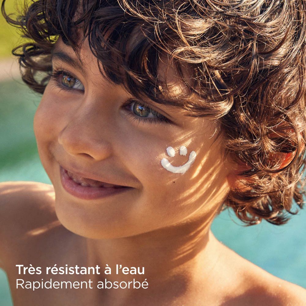 Un garçon avec un smiley de crème solaire sur le visage. Texte : Très résistant à l'eau, Rapidement absorbé.
