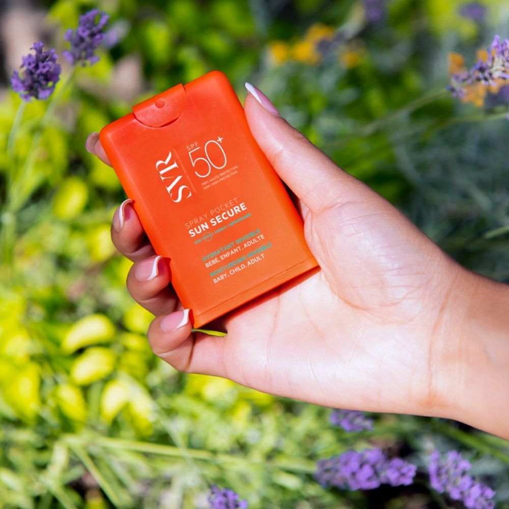 Main tenant un spray orange SPF 50+. Inscription: SVR, Sun Secure Spray Pocket. Pour bébés, enfants, adultes.