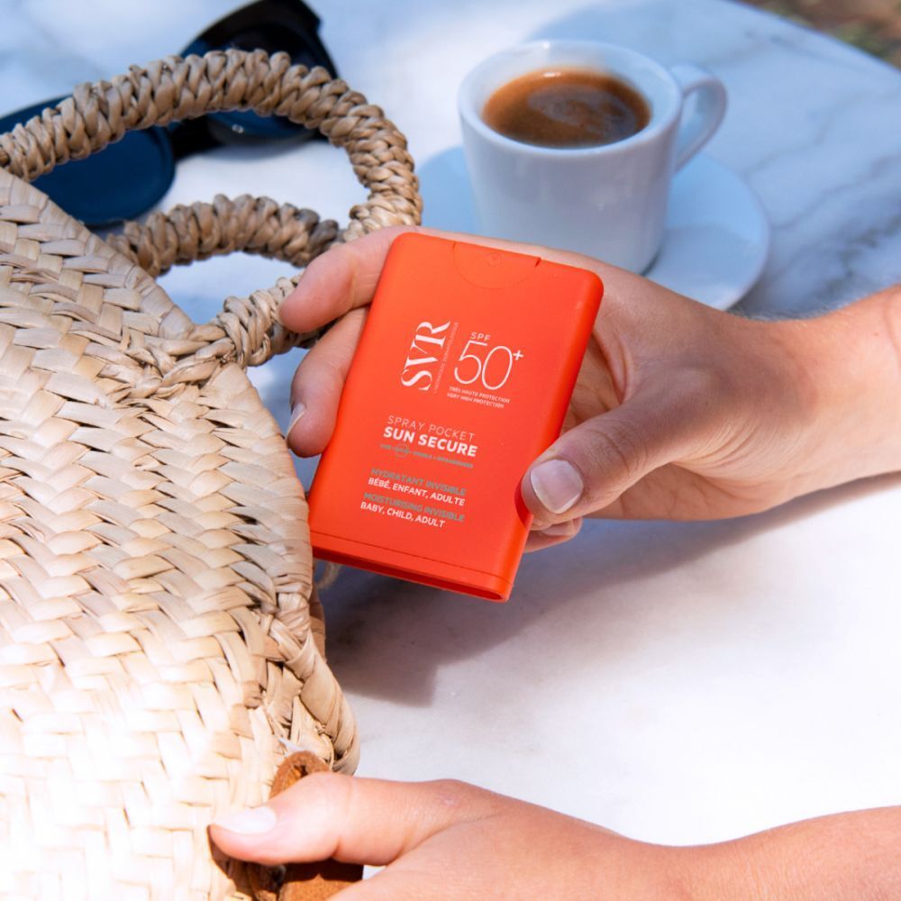 Main sortant un spray orange SPF 50+ d'un sac. Inscription: SVR, Sun Secure Spray Pocket.