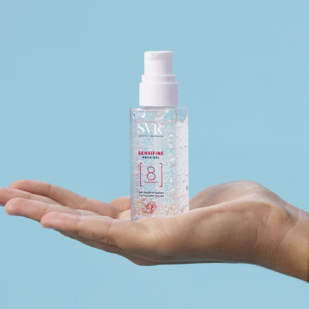 Een flesje SVR Aqua-Gel Sensifine in een hand. Transparante fles met witte pomp. Opschrift: SVR, Aqua-Gel, Sensifine, 8 Ingredients.